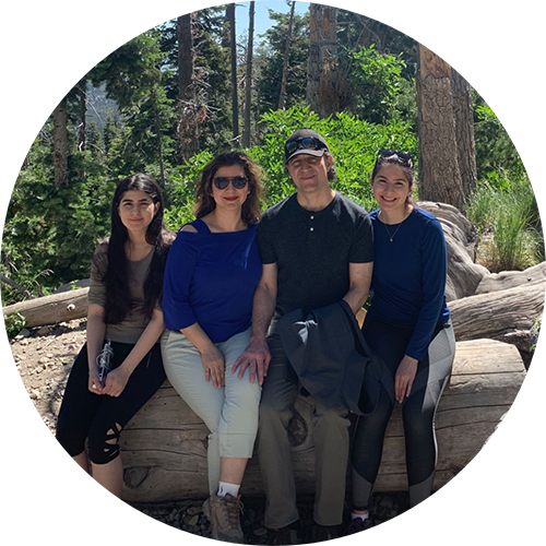Doctor Hejazi with his wife and two daughters sitting on a large log in a forest